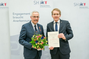 Ministerpräsident Daniel Günther übergab das vom Bundespräsidenten verliehene Verdienstkreuz am Bande und die Urkunde an Horst Wardius aus Steinhorst. (c) Foto: Frank Peter